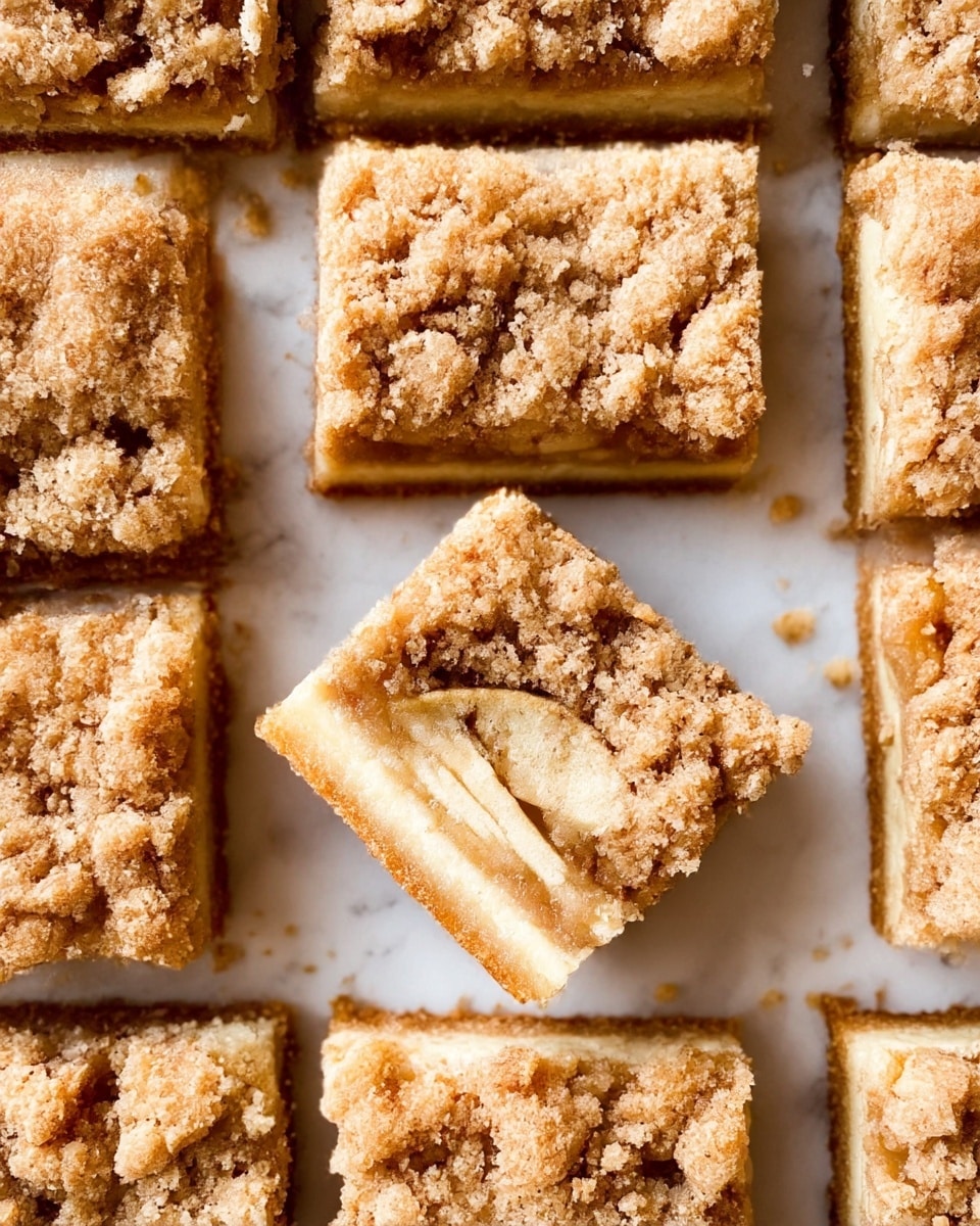 The image shows several square pieces of crumb cake arranged closely together on a white marbled surface, with one piece in the center turned on its side to reveal three main layers: a thick, golden-brown crumbly top layer with coarse granules; a middle layer of pale, soft, and moist apple slices; and a bottom layer of a light brown, dense cake or crust. The crumb topping appears rough and textured, while the apple layer looks juicy and tender, contrasting with the firm base. photo taken with an iphone --ar 4:5 --v 7