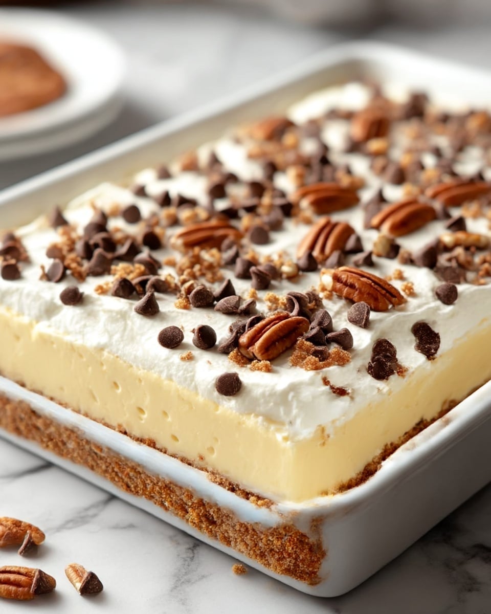 The image shows a square cake in a white baking dish with three visible layers: the bottom layer is a crumbly brown crust, the middle layer is a smooth pale yellow custard, and the top layer is a thick white whipped cream. On top of the whipped cream are scattered dark brown chocolate chips and small pieces of chopped nuts, creating a textured and crunchy look. The background has a soft focus and a white marbled texture. photo taken with an iphone --ar 4:5 --v 7