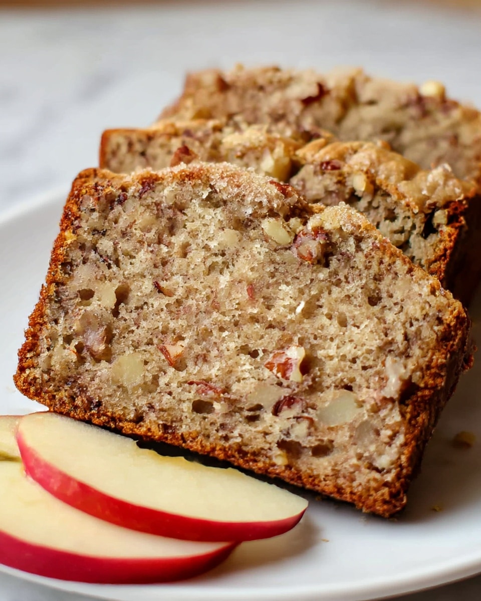 The image shows three thick slices of nut bread stacked closely on a white plate, with visible chunks of nuts embedded in the light brown, soft and crumbly texture of the bread. The edges of the bread have a darker, golden crust. At the front right side of the plate, a small piece of red apple is placed, adding a touch of fresh, smooth, and shiny contrast to the scene. The background is a white marbled texture, keeping the focus on the bread and apple piece. photo taken with an iphone --ar 4:5 --v 7