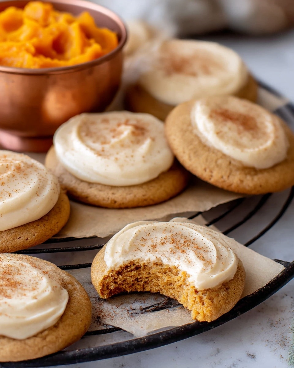 The image shows several pumpkin cookies arranged on a parchment-lined black cooling rack, placed on a white marbled texture surface. Each cookie has a thick base with a warm brown, slightly cracked texture, topped with a creamy layer of light beige frosting sprinkled with a fine dusting of brown spice. The closest cookie in the foreground has a bite taken out of it, revealing a soft crumb inside. In the background, there is a small bowl filled with bright orange pumpkin puree, adding a pop of color to the scene. Photo taken with an iphone --ar 4:5 --v 7