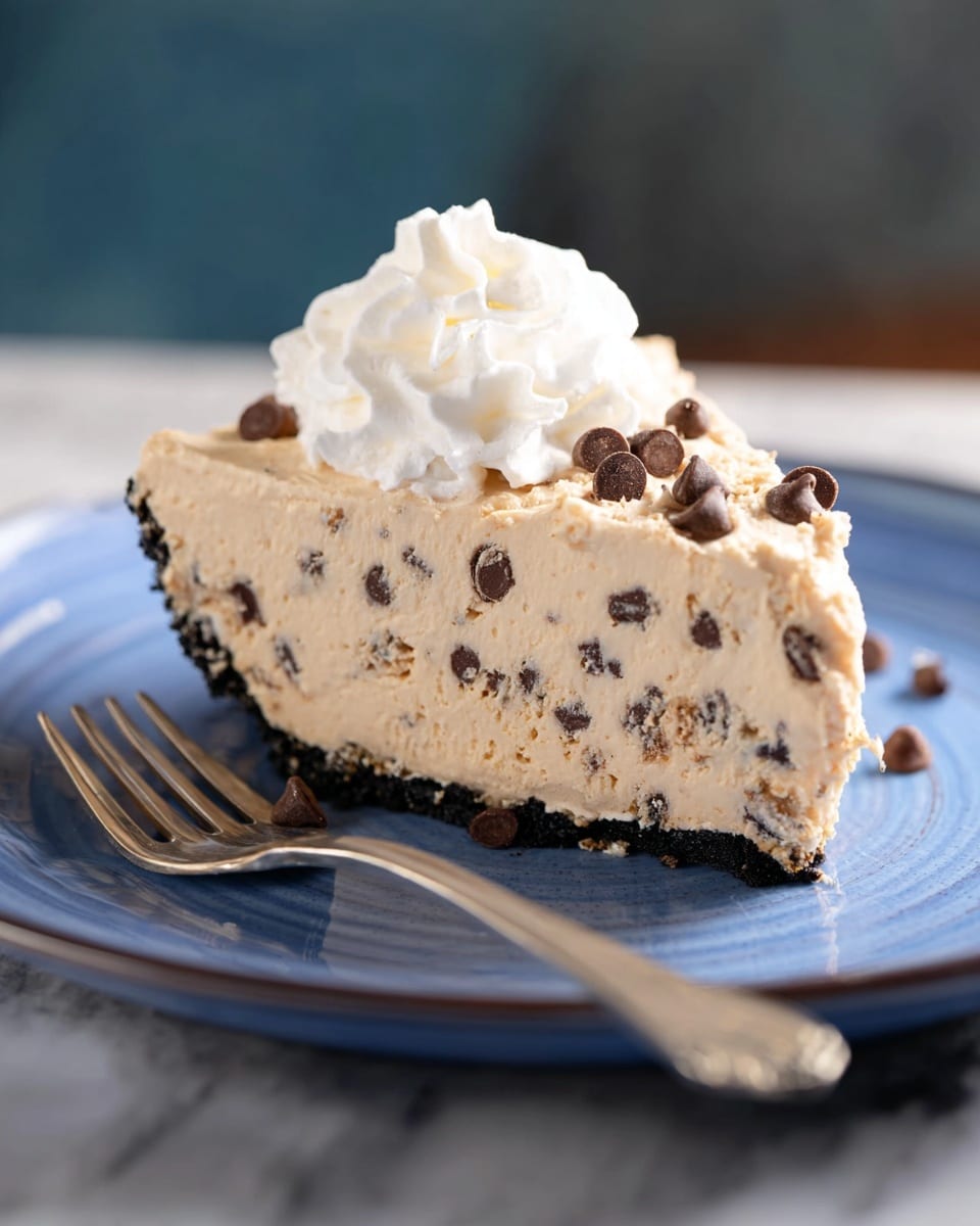 A slice of pie with three visible layers sits on a white plate with a blue interior. The bottom layer is a dark, crumbly crust. The middle layer is thick and creamy with a light tan color, filled with many small dark chocolate chips evenly spread throughout. The top layer is a fluffy white whipped cream dollop with extra chocolate chips scattered on it. A silver fork rests on the plate next to the pie slice. The plate is set on a white marbled surface in soft, natural light. Photo taken with an iphone --ar 4:5 --v 7