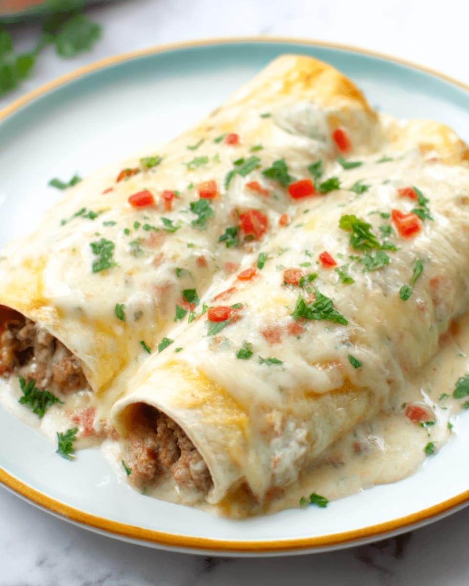 The image shows two rolled enchiladas placed side by side on a white plate. The enchiladas are covered in a smooth, creamy white sauce with visible small bits of cooked ground meat. On top, there is melted cheese that is slightly bubbly and covers most of the surface. There are small pieces of red chili and fresh green cilantro leaves sprinkled evenly over the sauce and cheese. The plate rests on a white marbled surface, and the photo taken with an iphone --ar 4:5 --v 7