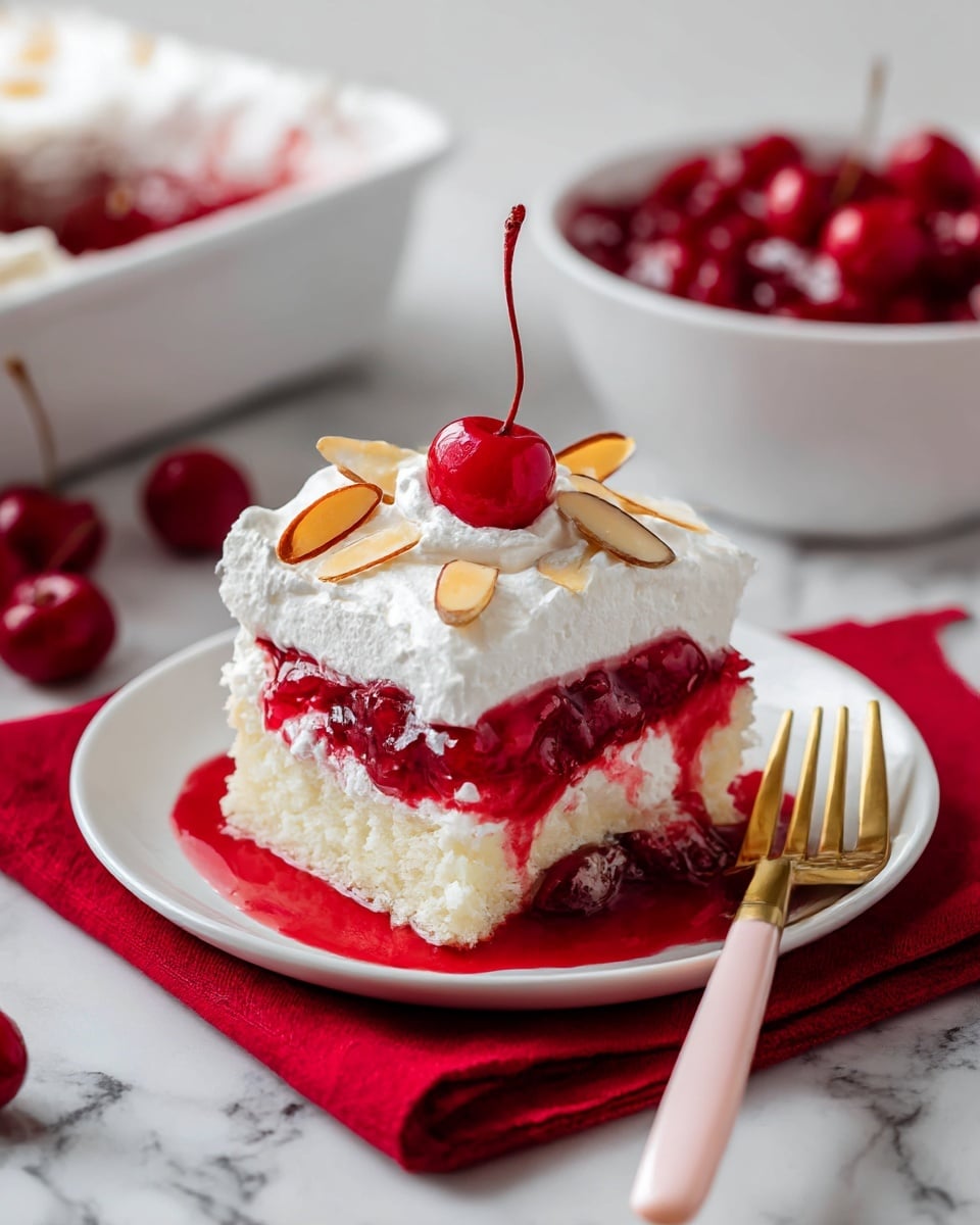 A slice of layered cherry dessert sits on a white plate over a red cloth. The bottom layer is white sponge cake soaked with a glossy, deep red cherry filling that contains whole cherries. Above this is a thick layer of smooth, pale yellow custard or cream. The top layer is fluffy white whipped cream, decorated with a shiny red cherry in the center and a few thin almond slices scattered on it. A gold fork with a pink handle rests beside the dessert. In the background, a white bowl with more bright red cherries and another slice of the dessert on a white plate are visible, all placed on a white marbled surface. Photo taken with an iphone --ar 4:5 --v 7