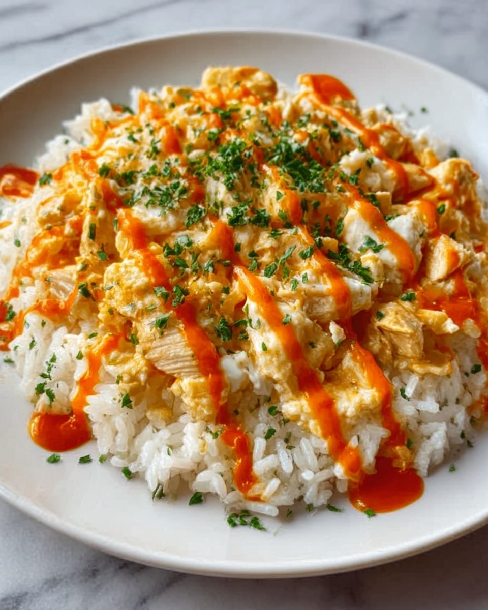 The image shows a white plate filled with a base layer of white rice, topped with scrambled eggs mixed with small white pieces of chicken. The eggs and chicken cover the rice evenly, creating a soft, creamy texture with light yellow and white colors. This layer is drizzled with an orange sauce in thin stripes, and finely chopped green herbs are sprinkled on top, adding a touch of green. The plate sits on a white marbled surface. Photo taken with an iphone --ar 4:5 --v 7