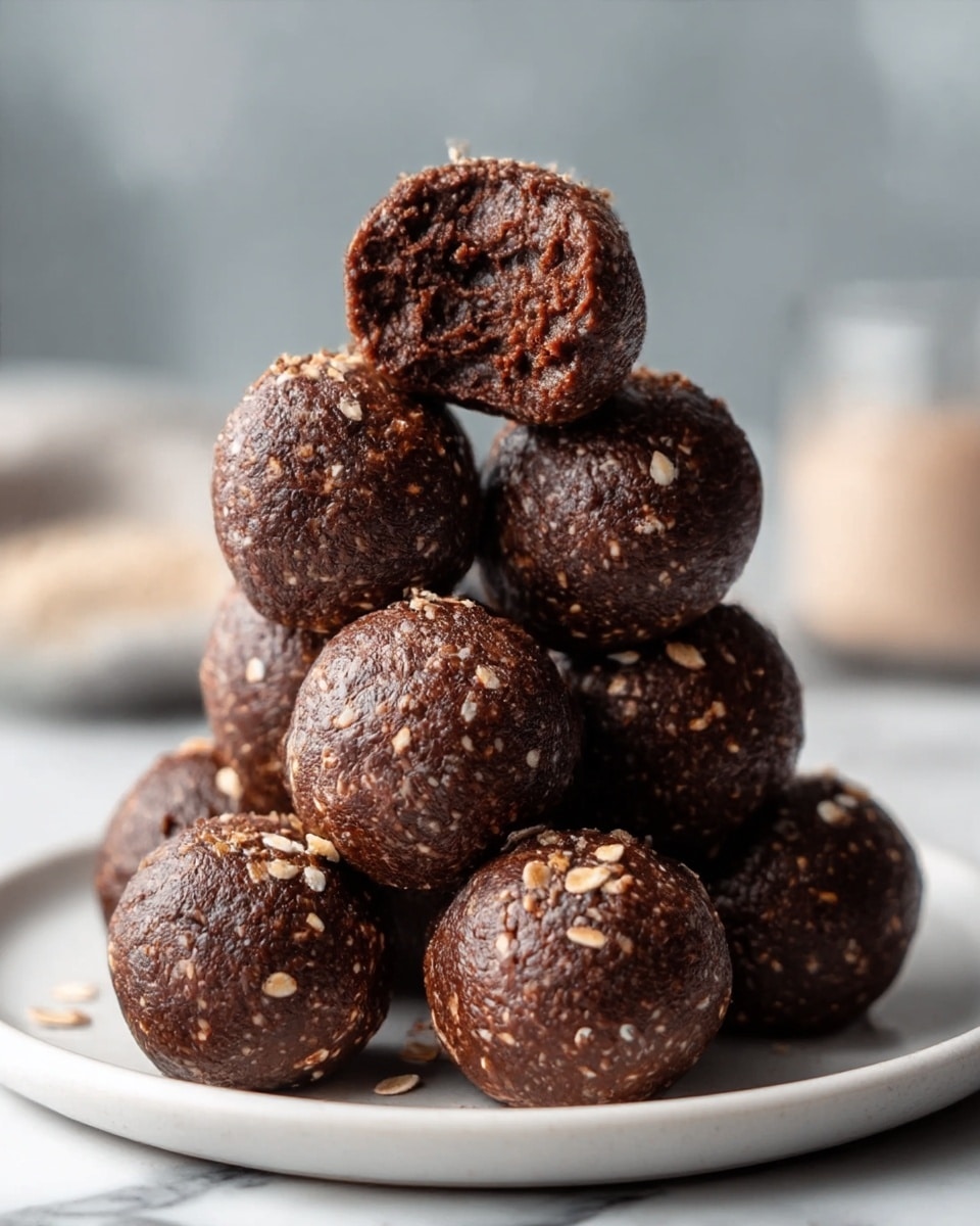 A stack of eight round chocolate balls is shown on a white plate, arranged in a pyramid shape with five balls at the bottom, two in the middle, and one on top. Each chocolate ball is dark brown with a rough texture and small bits of oats sprinkled on the surface. The top ball has a bite taken out, revealing a moist, dense dark chocolate inside. The plate sits on a white marbled surface, with a blurred background that has soft, neutral colors. Photo taken with an iphone --ar 4:5 --v 7