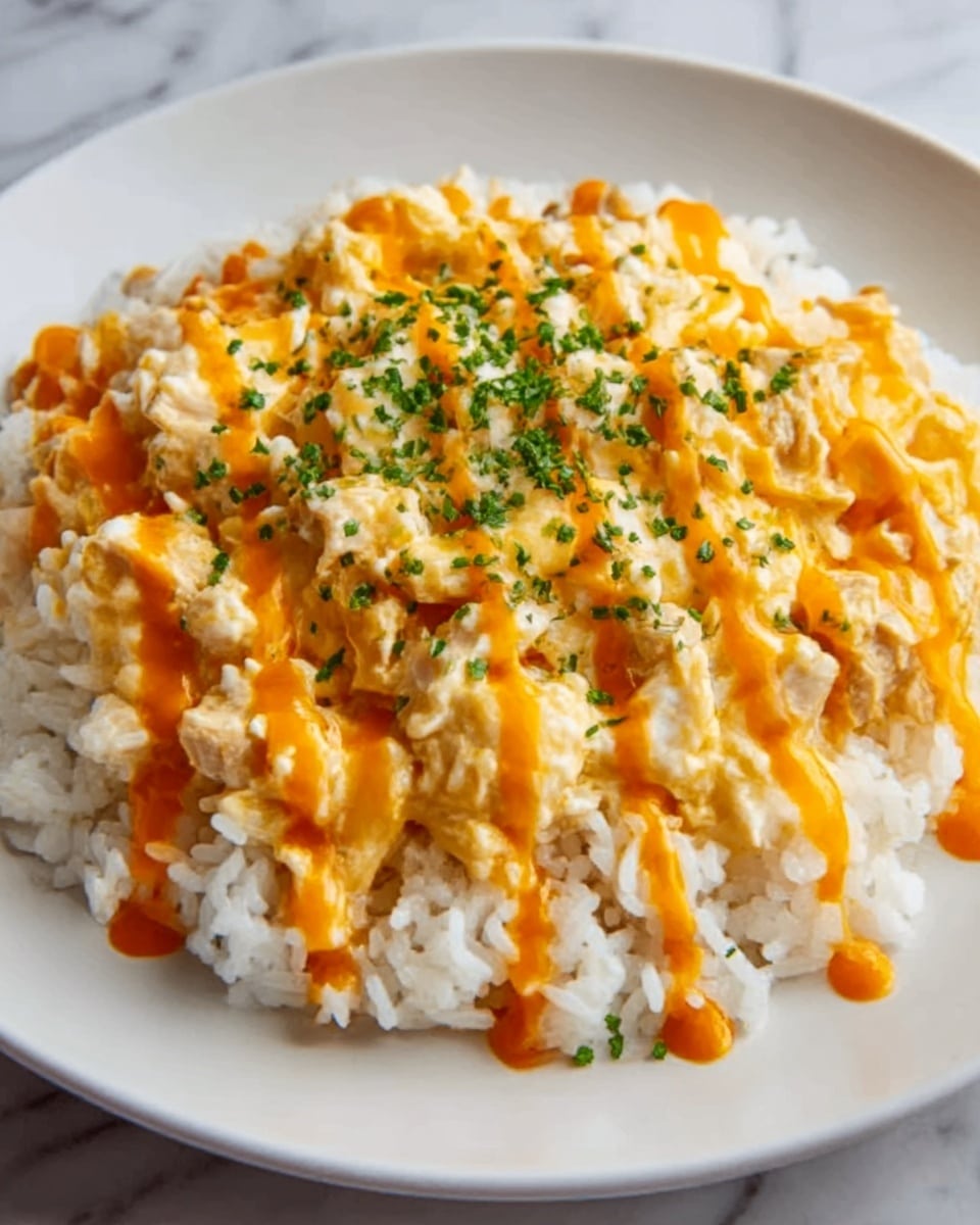 The image shows a white plate filled with a base layer of cooked white rice, soft and slightly sticky in texture. On top of the rice is a thick layer of creamy scrambled eggs mixed with small pieces of chicken, with a light yellow and white color showing. The dish is drizzled with a bright orange sauce evenly across the top, adding a shiny texture, and sprinkled with finely chopped green herbs for a hint of color contrast. The plate is placed on a white marbled surface. photo taken with an iphone --ar 4:5 --v 7