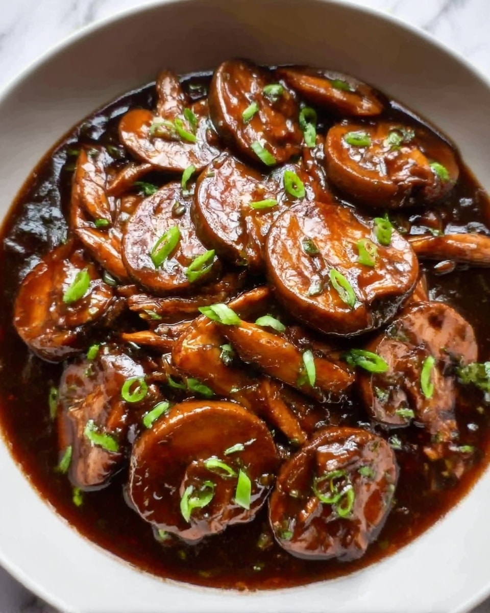A close-up image shows a bowl filled with glossy brown sauce-covered shiitake mushrooms, layered evenly and garnished with small green chopped chives scattered on top. The mushrooms have a shiny, smooth texture with a rich brown color, sitting in a shallow pool of thick sauce. The bowl is white, placed on a white marbled surface. photo taken with an iphone --ar 4:5 --v 7