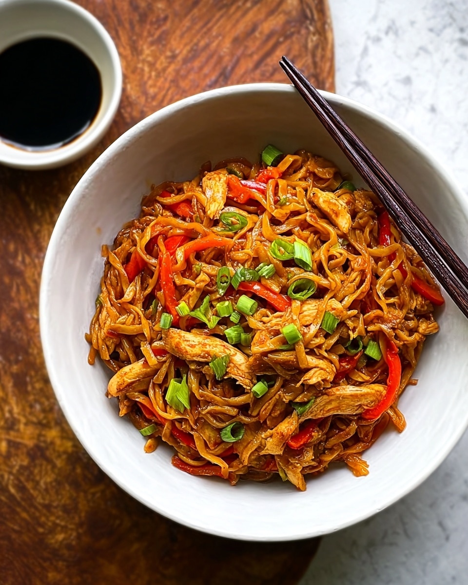 The image shows a close-up of cooked noodles mixed with strips of cooked chicken and green chili slices, all coated in a glossy, reddish-brown sauce. The noodles are curly and soft, with an even sauce covering, and the chicken pieces are tender and slightly shiny. The green chili slices are scattered throughout, adding pops of bright green color. A wooden spoon is lifting a portion of the noodles and chicken, showing the texture and coating of the sauce. The dish is in a dark pan which contrasts with the vibrant colors of the food. photo taken with an iphone --ar 4:5 --v 7