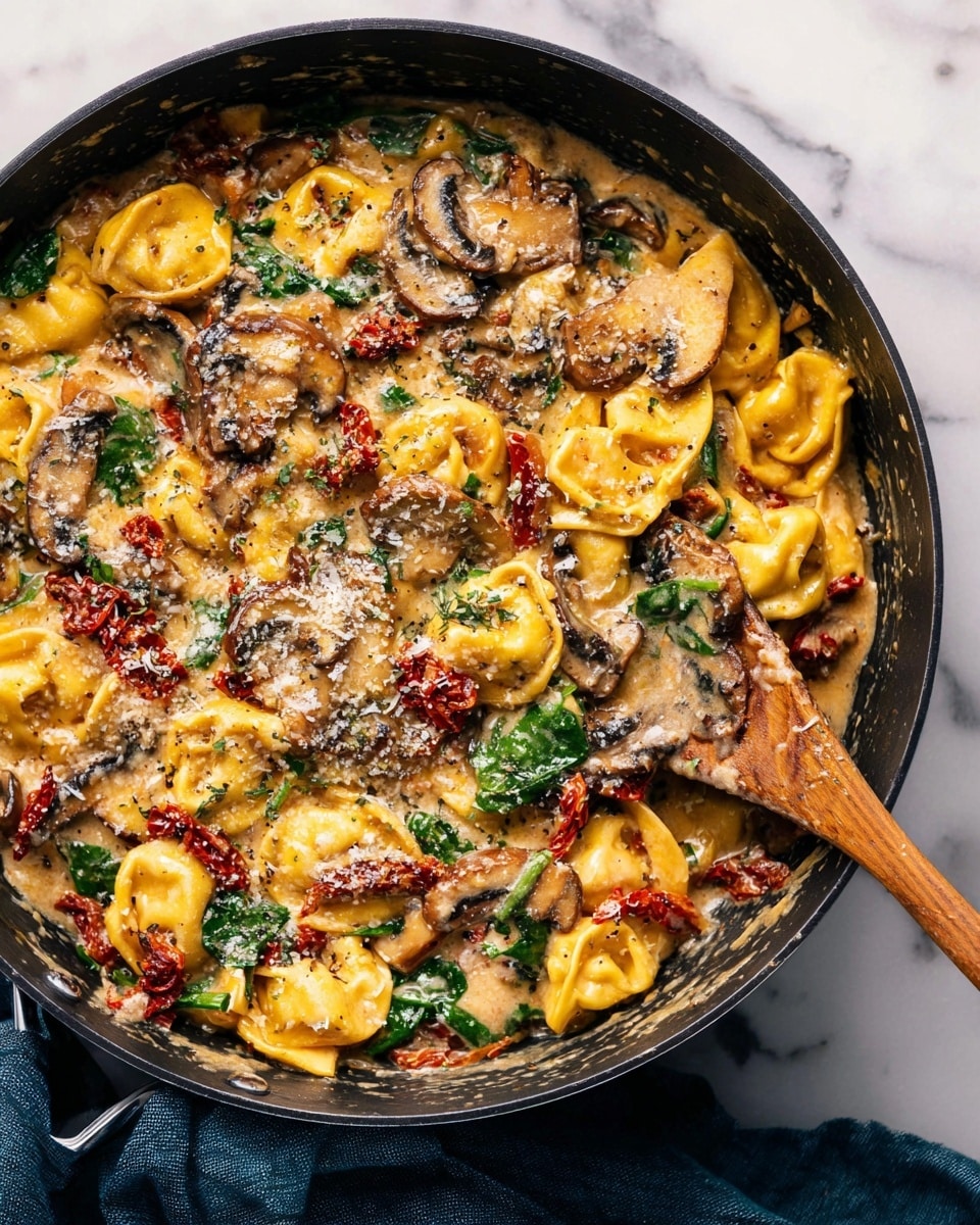 A thick, creamy pasta dish is shown in a black pan on a white marbled surface. The pasta, which appears to be yellow tortellini, forms the main base layer with its soft, slightly shiny texture. Mixed into this are cooked mushroom slices that add a brown, wrinkled layer across the surface. Sun-dried tomatoes, deep red and slightly wrinkled, are scattered throughout, adding color contrast. Fresh spinach leaves provide a bright green layer that peeks through the sauce. The entire dish is coated in a glossy, bubbly cheese sauce with melted cheese strands and sprinkled with grated parmesan. A wooden spoon is placed inside the pan, stirring the ingredients. A dark blue cloth is partially visible beside the pan. Photo taken with an iphone --ar 4:5 --v 7