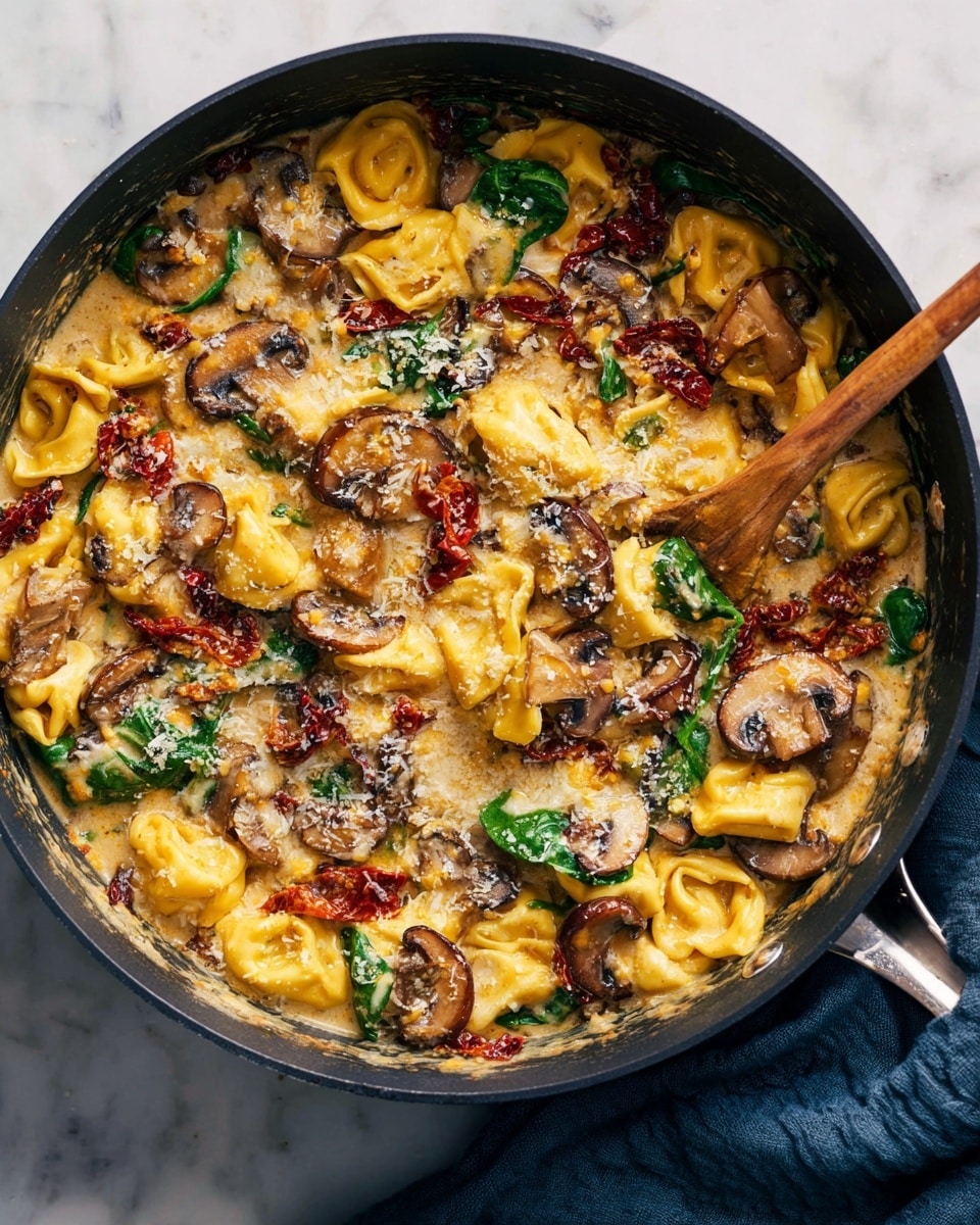 A close-up view of a creamy pasta dish in a black pan on a white marbled surface, showing three main layers: the base layer of yellow tortellini pasta, the second layer of sautéed brown mushrooms and green spinach leaves scattered throughout, and the top layer covered with creamy sauce mixed with bits of red sun-dried tomatoes and grated cheese, giving a glossy texture. A wooden spoon is partially submerged on the left, stirring the dish, and a piece of blue cloth is visible on the right side of the pan. Photo taken with an iphone --ar 4:5 --v 7